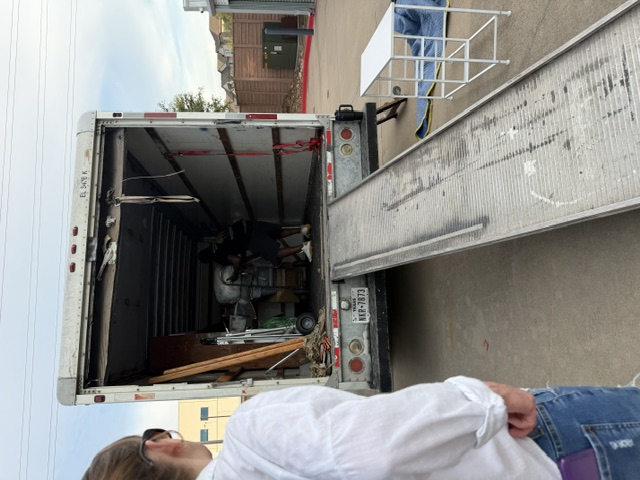 Moving truck with open cargo door and ramp, person in white shirt viewing contents