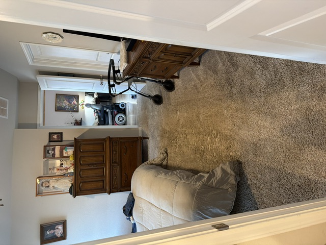 Bedroom with bed, wooden furniture, doorway to bathroom with mobility equipment, and carpet flooring