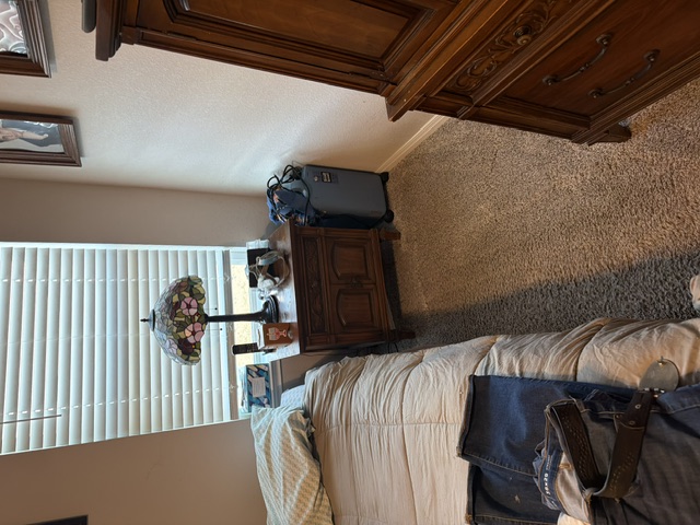 Bedroom with wooden furniture, bed, nightstand with lamp, suitcases, and window with blinds