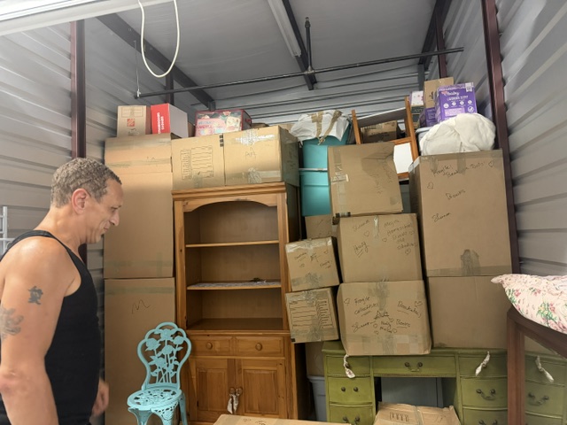 Man standing in storage unit filled with cardboard boxes and furniture