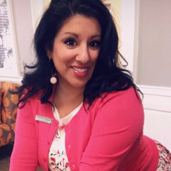 Professional woman in bright pink cardigan smiling at camera indoors