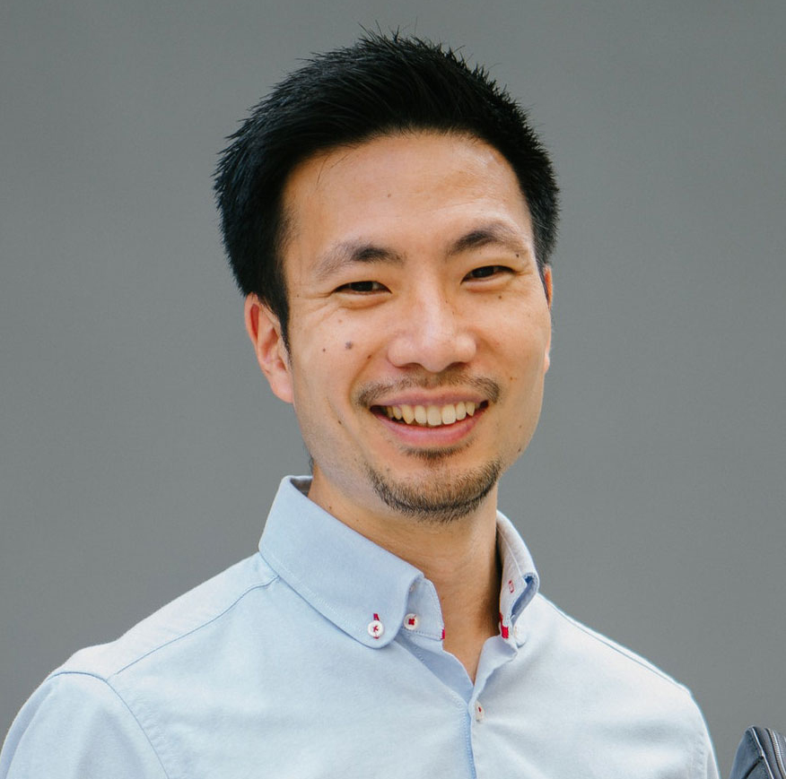 Man in light blue button-up shirt smiling at camera against gray background