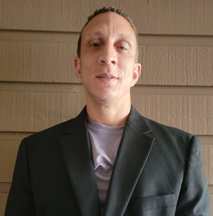 Man wearing dark blazer and gray shirt against textured beige wall background